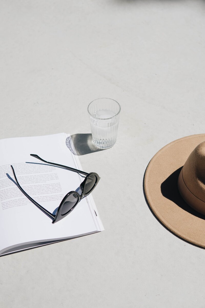 Sunglasses, notebook, and hat on a sunny table