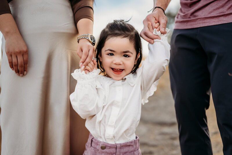 Mom lifts her baby and smiling. Sun shines behind her.