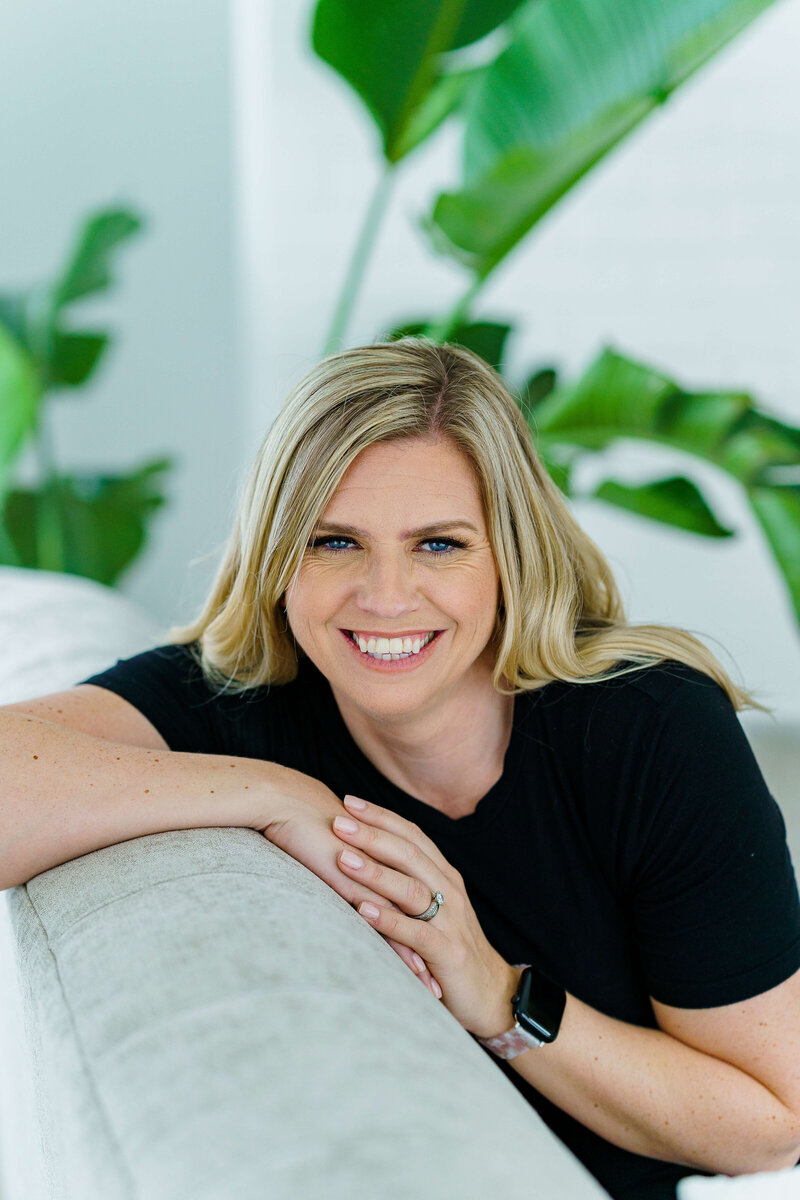 Photographer leaning over back of sofa wearing black top with green in background