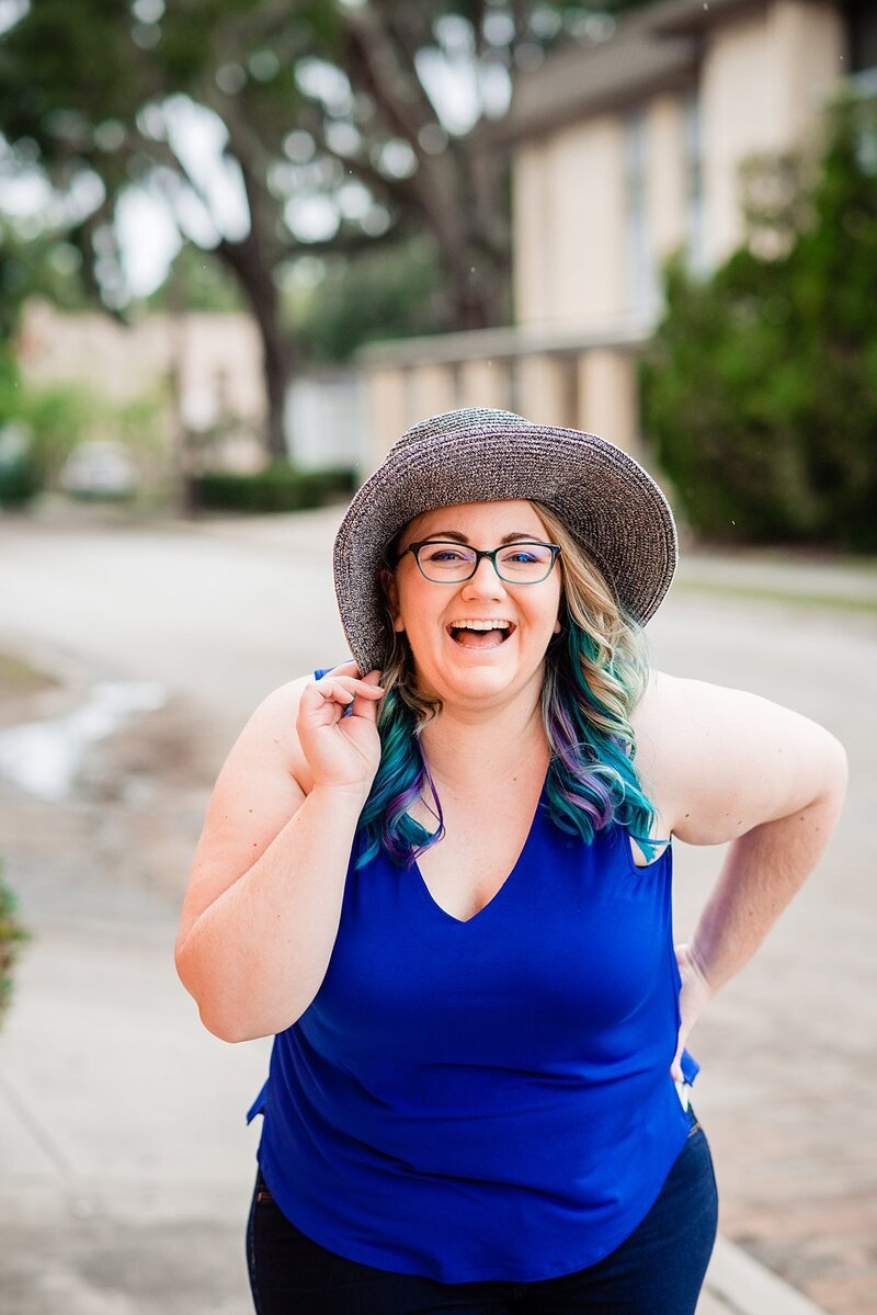 Mahlia wearing a cobalt blue top laughing at the camera while holding onto her sunhat