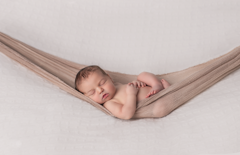 "Newborn baby boy sleeping in a neutral-colored hammock during a studio photography session in Ottawa"