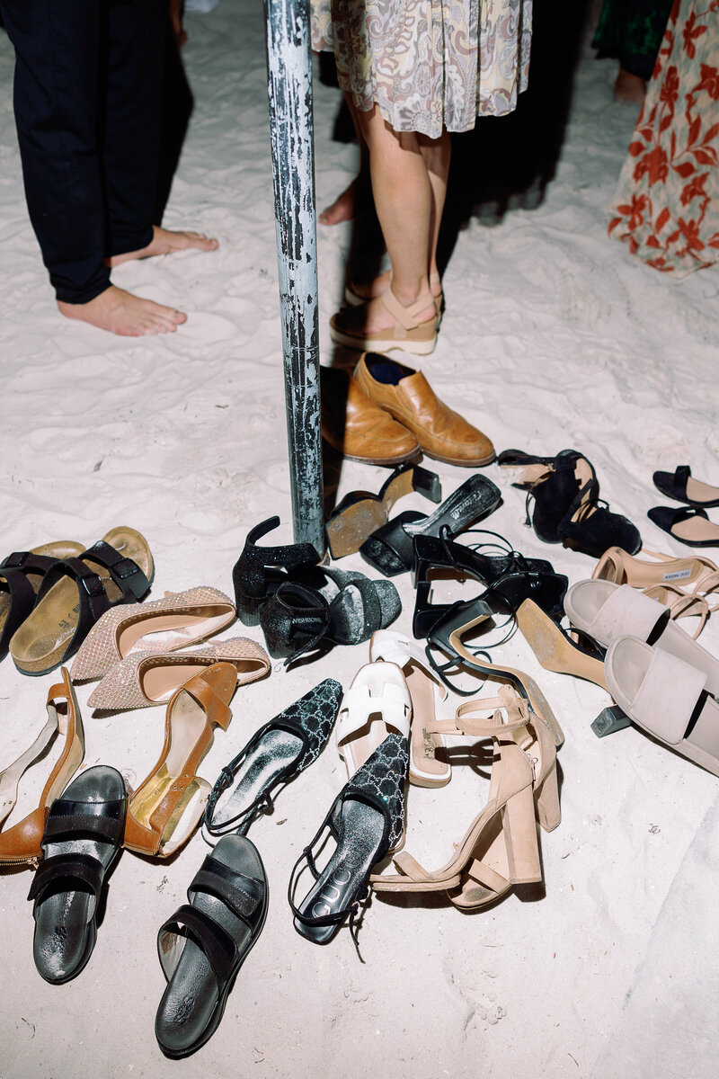Pile of wedding shoes and heels in the sand at the beach.