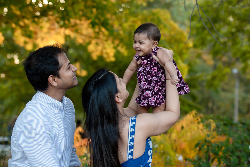 st-louis-fall-mini-session-mom-with-dad-holding-up-baby-girl-with-fall-leaves-at-forest-park