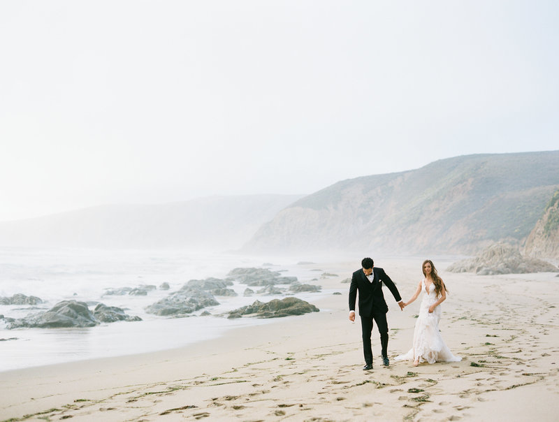 couple walking at point reyes beach with cliff coastline and wind blowing in hair