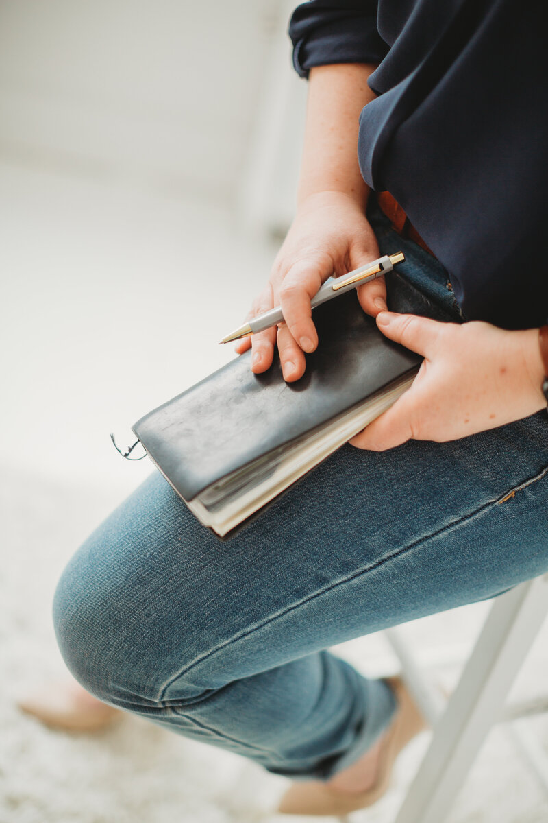 A closed notebook and a pen holding in hands