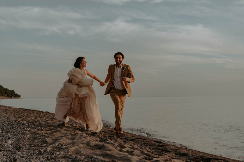 Bride and groom running on beach on wedding day in Goderich