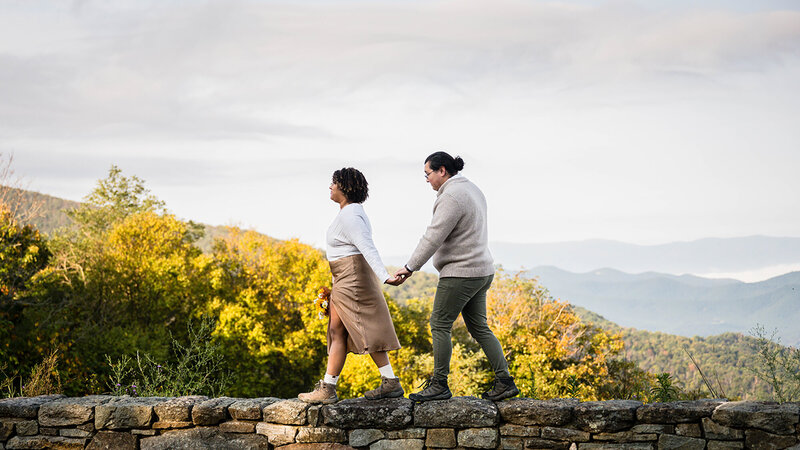 A couple hold hands while walking together on a stone wall in Shenandoah National Park on their elopement day.