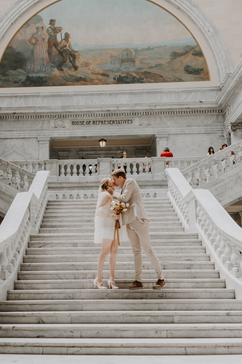 bride and groom standing in front of city hall while kissing