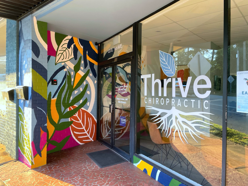 Thrive Chiropractic's logo grandly displayed in their large front window, surrounded by a colorful mural.