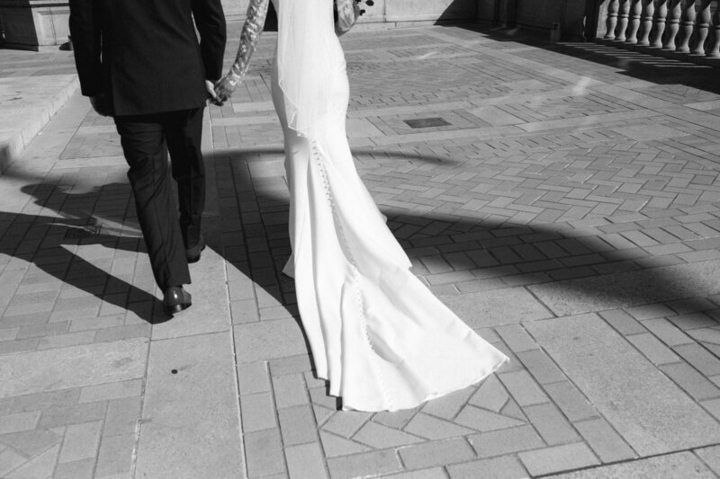 Black-and-white image of newlyweds walking hand in hand