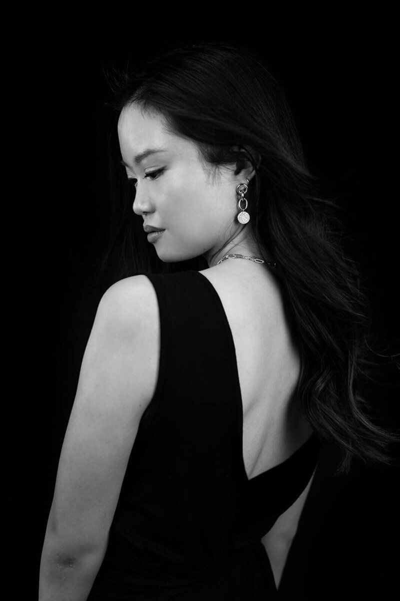 Black and white portrait of a girl from the back looking down her shoulder.She is wearing a black jumpsuit and important jewelry