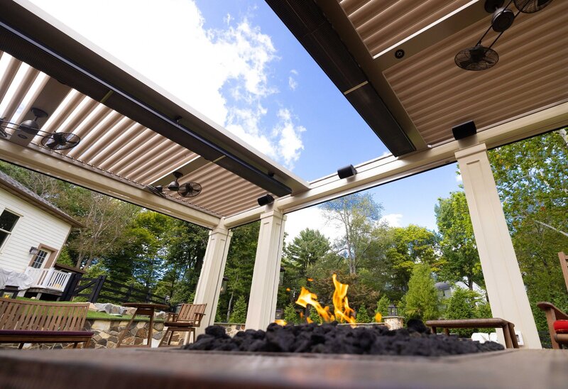 Low-angle view of a StruXure Slide pergola through a lit fire table. 