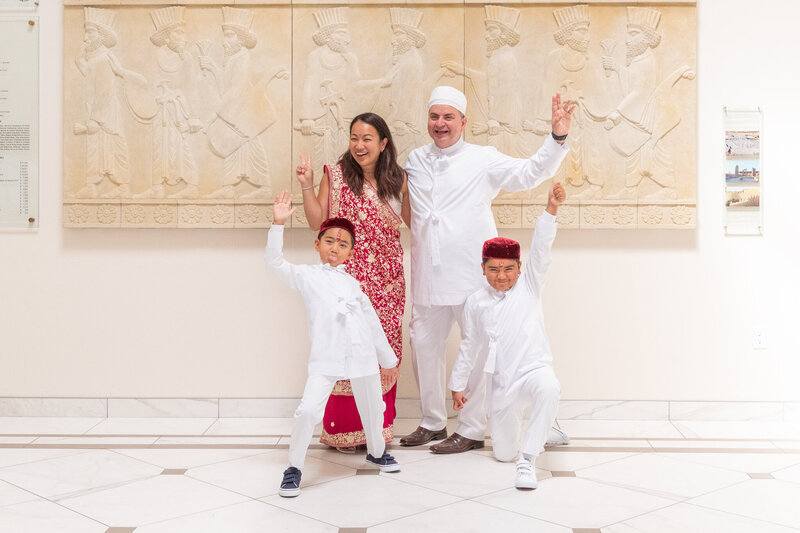 A family of 4 posing and laughing after a Navjote ceremony at a Zoroastrian temple.