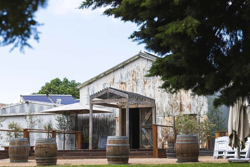 The entrance to a rustic barn with wine barrels out the front