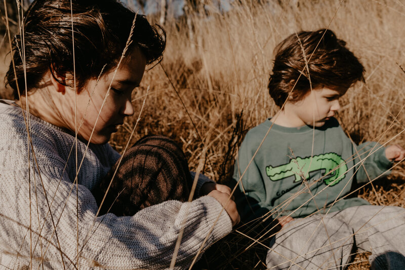 Twee jongens zitten in hoog gras en lezen samen een boek, omringd door de natuur.