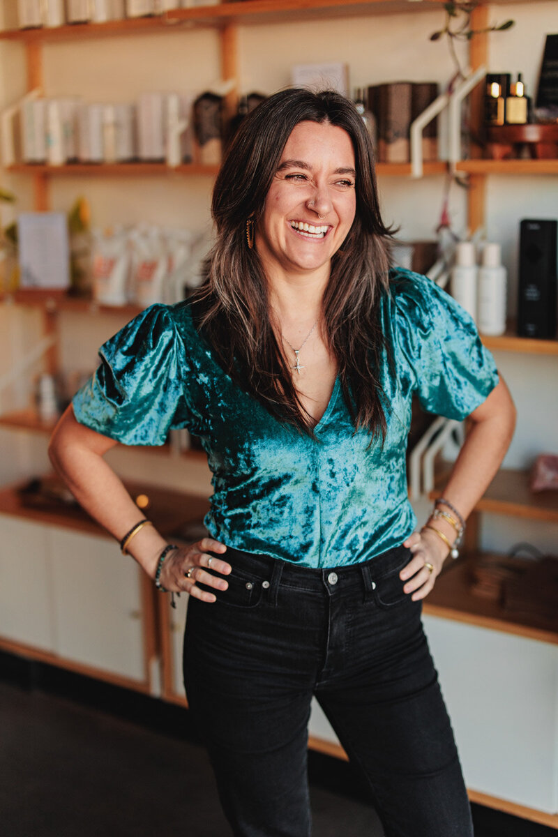 Chelsea a hair stylist in Eugene stands with her hands on her hips and smiles at the camera.