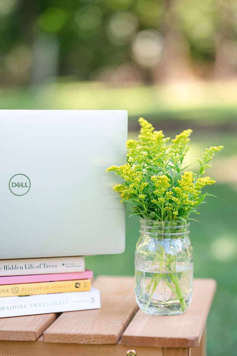A computer sits on a stack of books on a table with yellow flowers