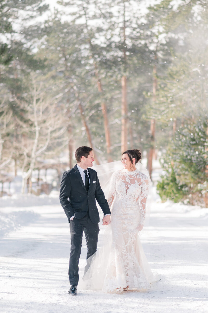 Bride and groom hold hands and walk down a snowy lane on their wedding day.