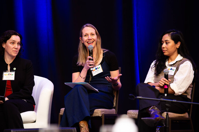 A photo of a blonde woman in a blue suit talking into a microphone as part of a panel discussion during a multi-day corporate conference.  Captured by Ottawa Event Photographer JEMMAN Photography COMMERCIAL
