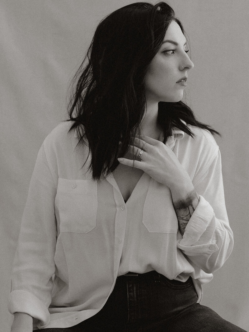Self‑portrait of the owner and main photographer of Acrewood Creative Studio who specializes in wedding & lifestyle photography in the Ottawa, Toronto and Montreal areas. She is wearing a white button-down shirt and black jeans, with hair blowing in wind.