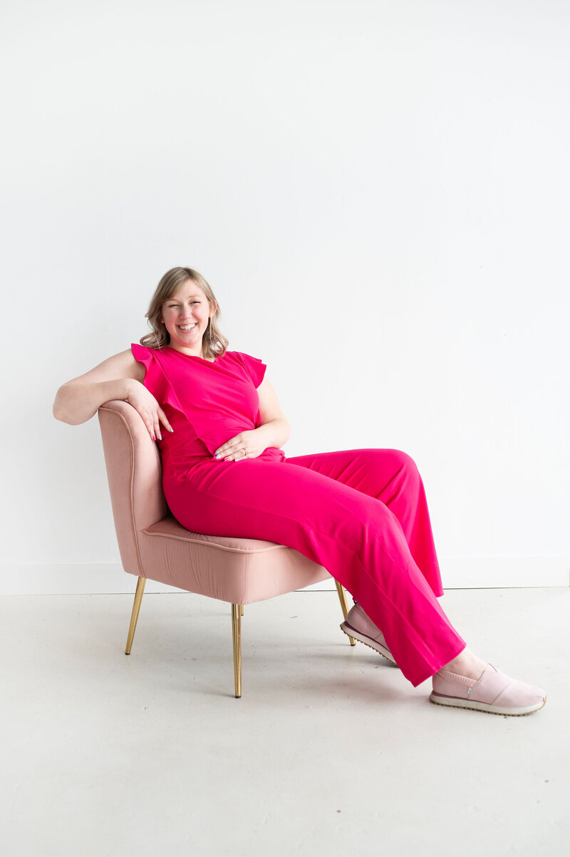 Kat Murphy in a pink jumpsuit sitting in a pink chair