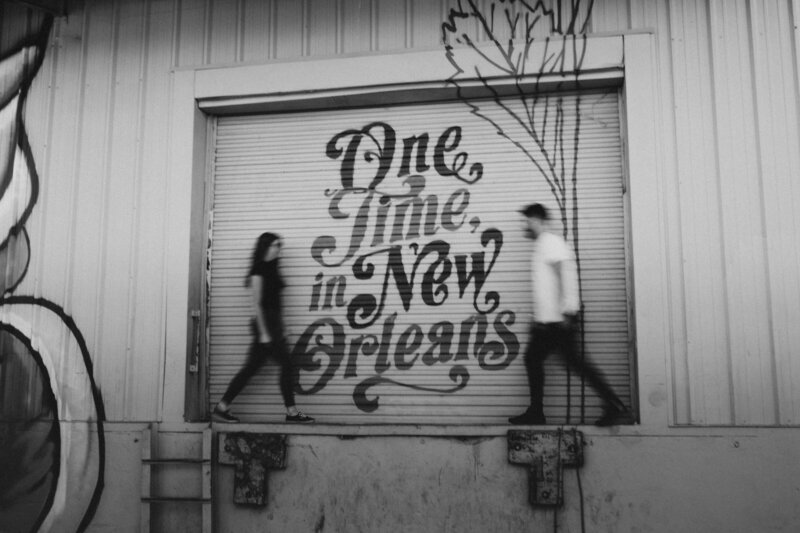 A couple walking in front of an industrial garage door with the words "One time in New Orleans" written on it.