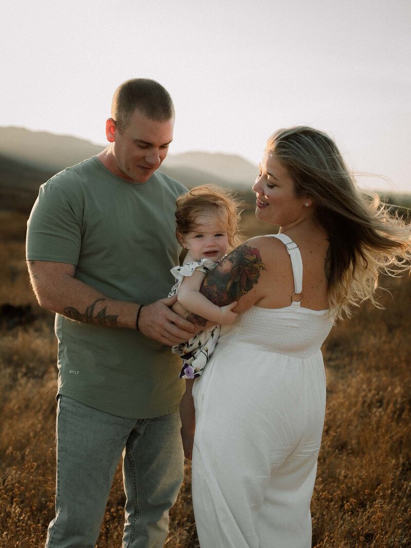 Parents holding their toddler in a sunlit field, laughing together during golden hour.