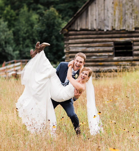a groom carries his bride through a field of wildflowers at their mountain elopement in the cascade mountains