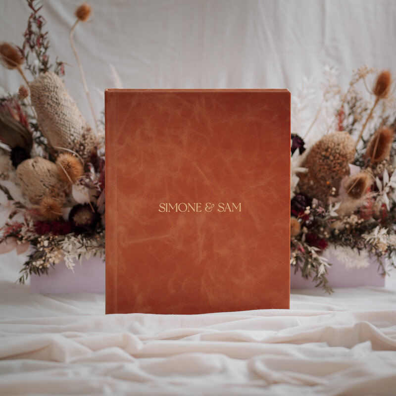 Tan leather wedding album in front of dried flower arrangement