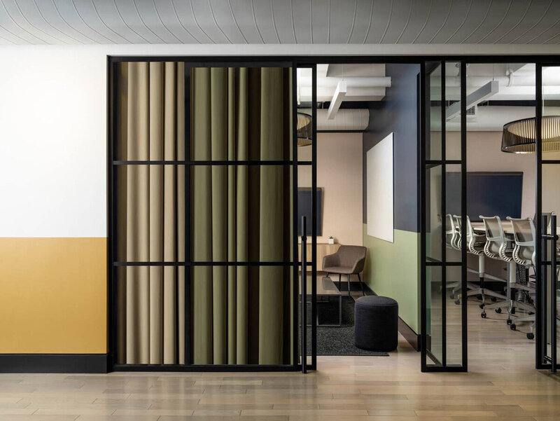 Conference room with glass partitions, muted green walls, and modern black-framed doors for a sleek interior design.
