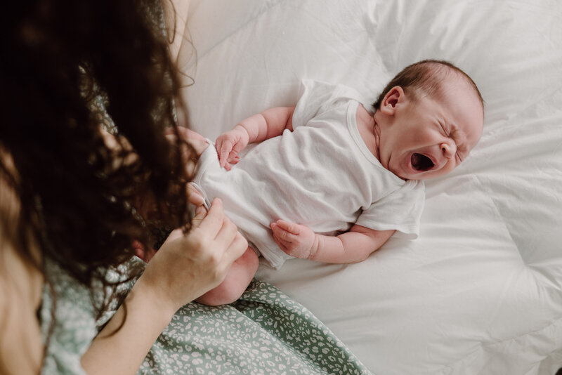 Motherhood photo of mom looking at baby boy yawning while wearing white in a lifestyle studio in Maryland.