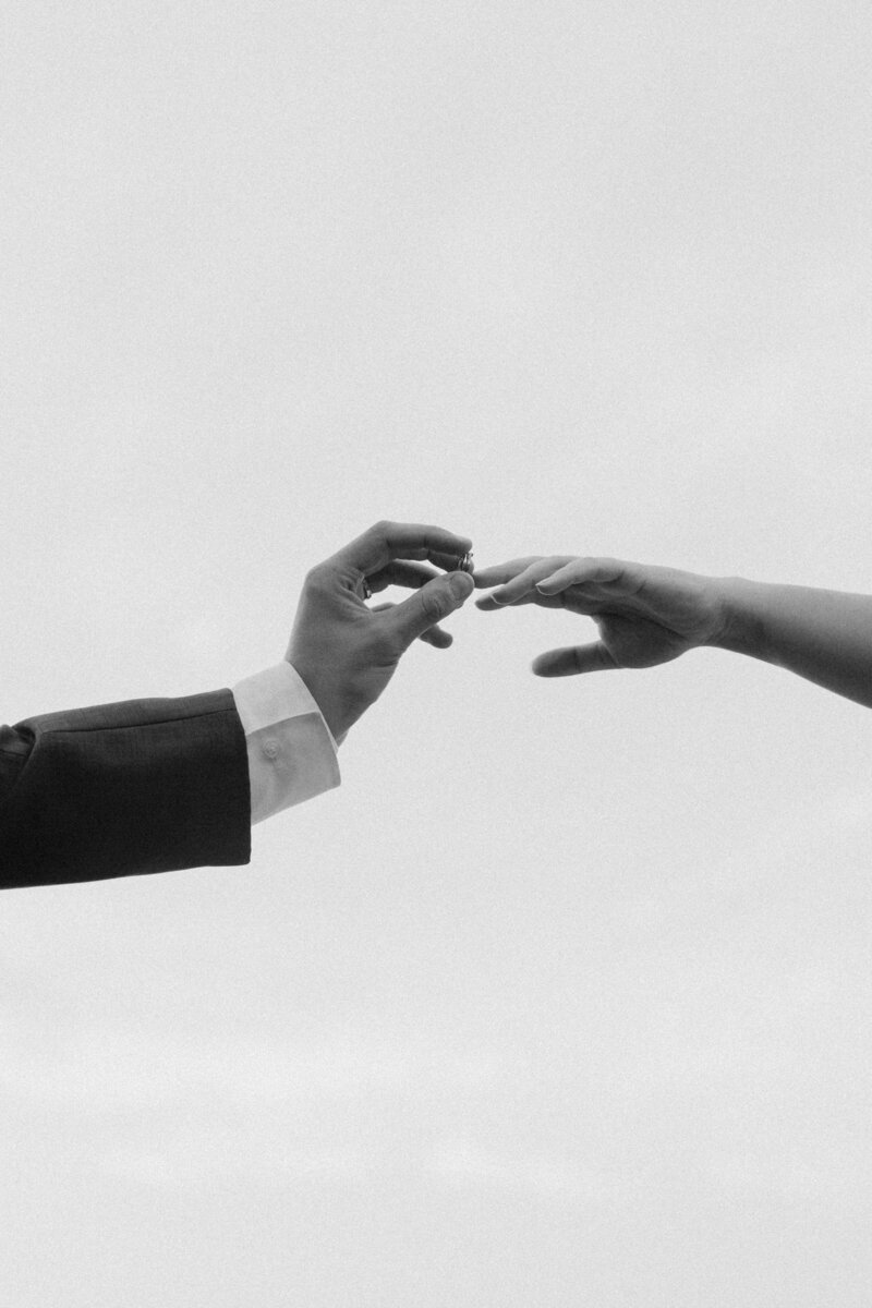 Adventurous wedding photographer captures eloping couple raising their rings toward the sky.