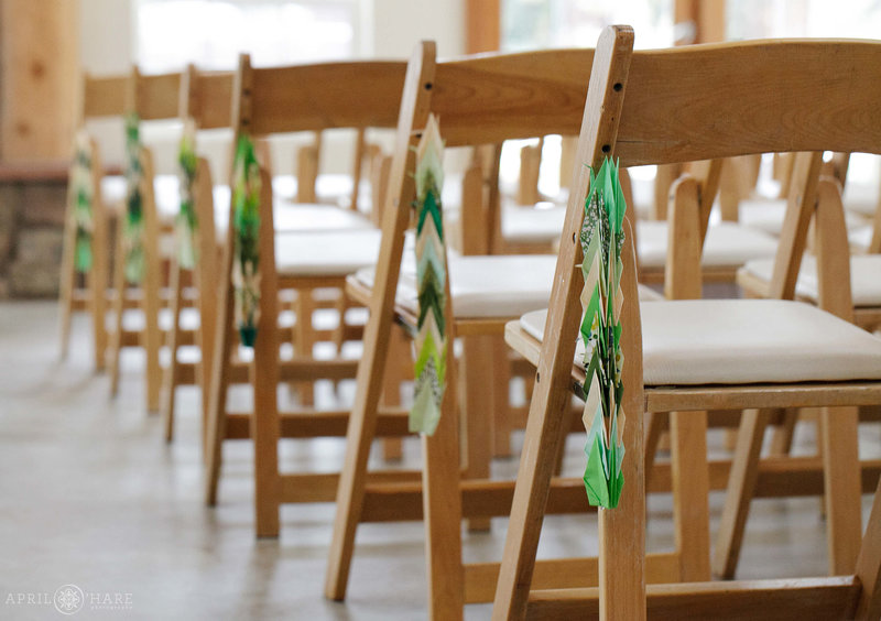 Wood folding chairs decorated with green paper cranes at an indoor fall wedding on a snowy day at Meadow Creek Lodge & Event Center in Pine Colorado