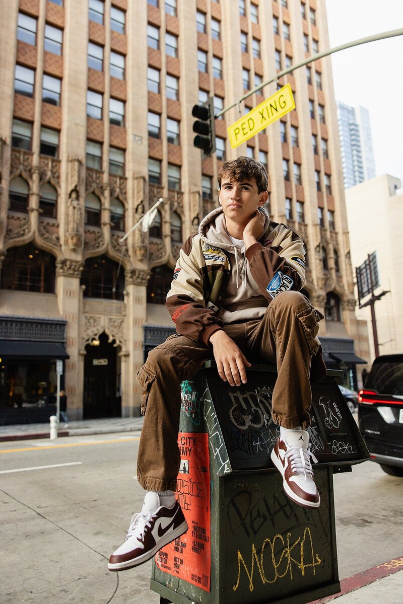 Senior guy sitting on a graffiti-covered utility box in Downtown Los Angeles during his urban senior portrait session