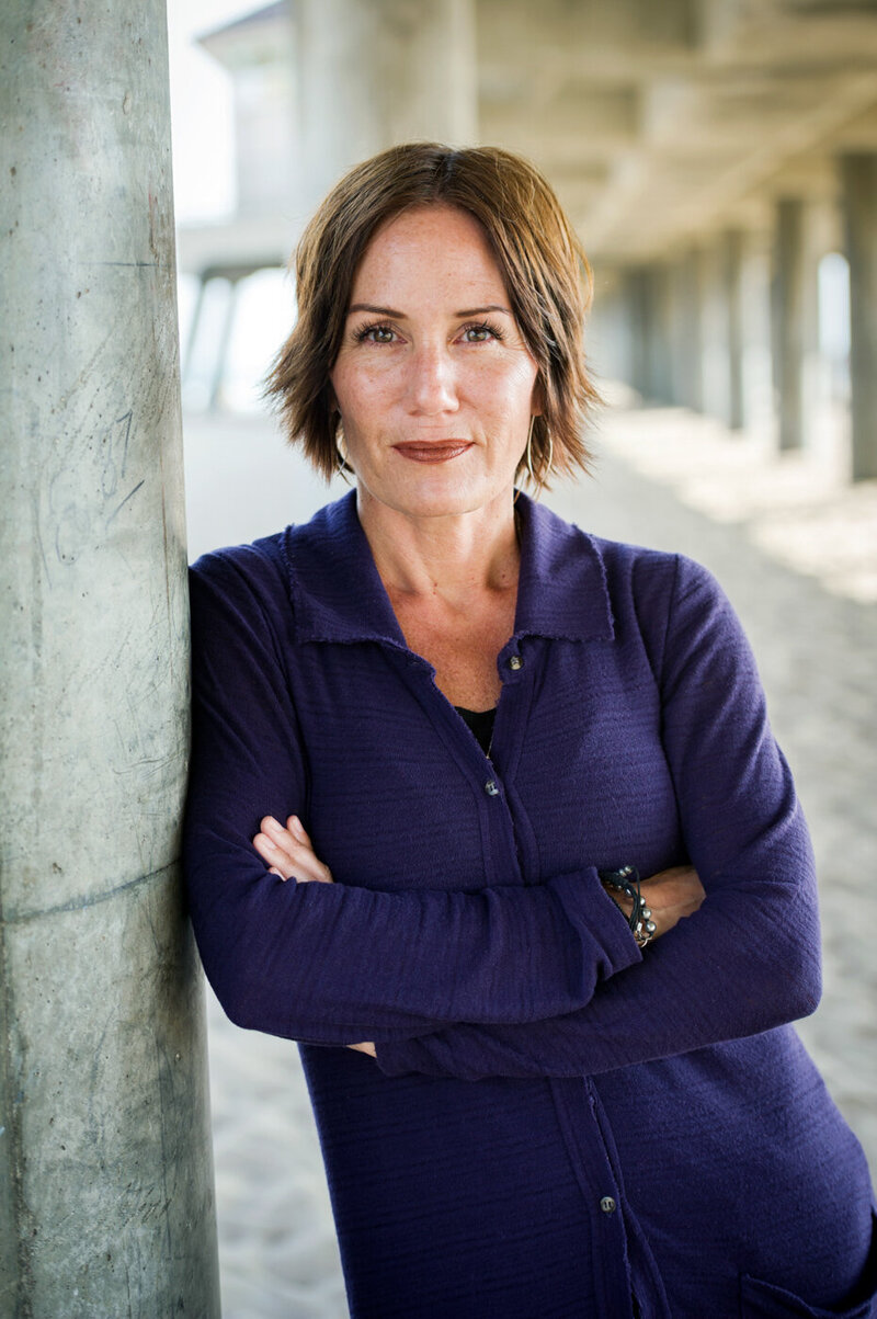 Headshot of Christina Haakenson of Juve Creative, posed under Huntington Beach pier, wearing purple collared shirt.
