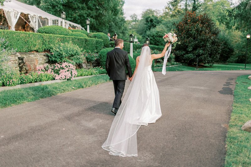 Bride and groom walking away from camera with bride holding up bouquet in celebration