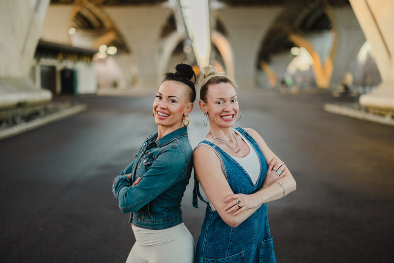 Two people standing back to back with their arms crossed smiling 