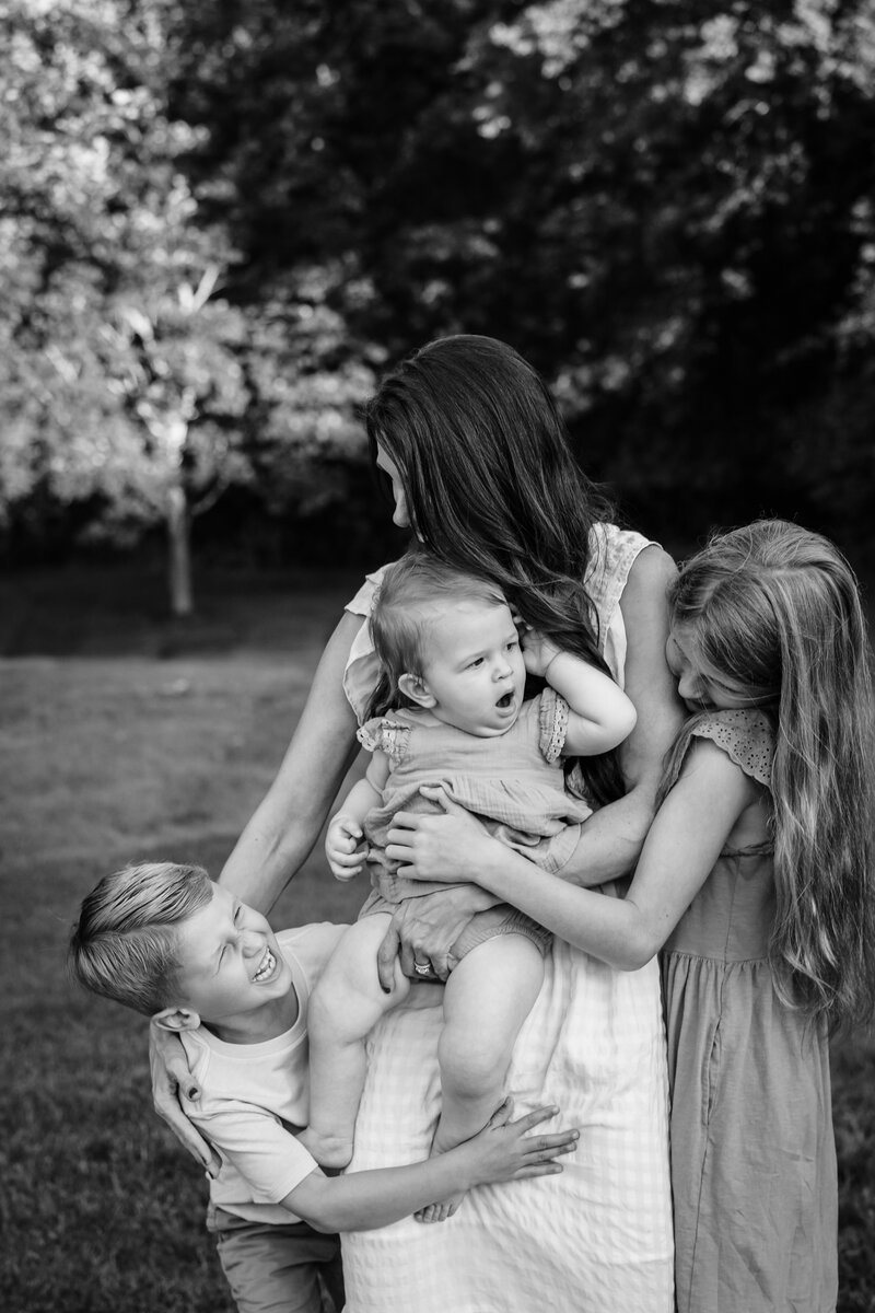 A black and white image of a mother holding a baby with two young children, a boy and a girl, embracing her from both sides.