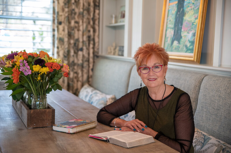 Jane Shine, sitting in her house, with her Bible open and a bouquet of flowers next to her