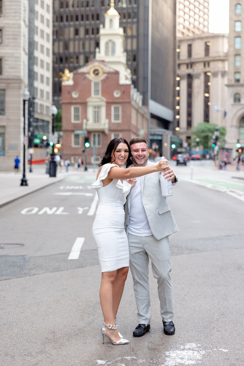 an engaged couple popping open a bottle of champagne in downtown Boston