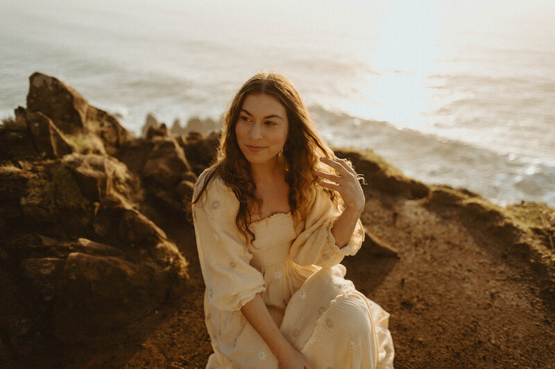 girl in white dress sitting on oregon coast cliffside