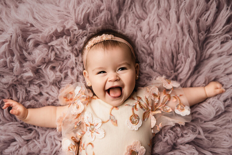 Adorable baby girl laying on a purple rug laughing