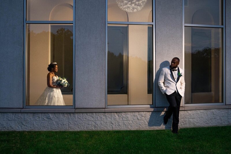 Bride and groom share a romantic moment through large windows at Duneland Falls Banquet Center