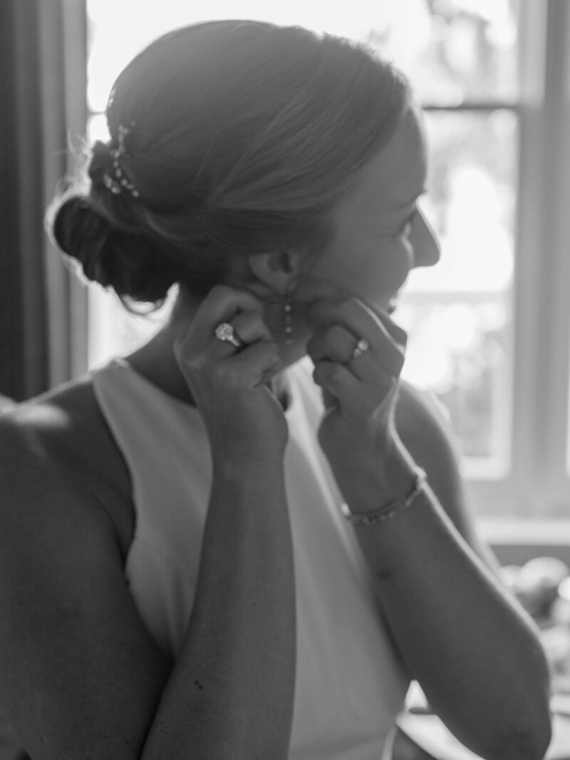 black and white photo of bride putting on her earings