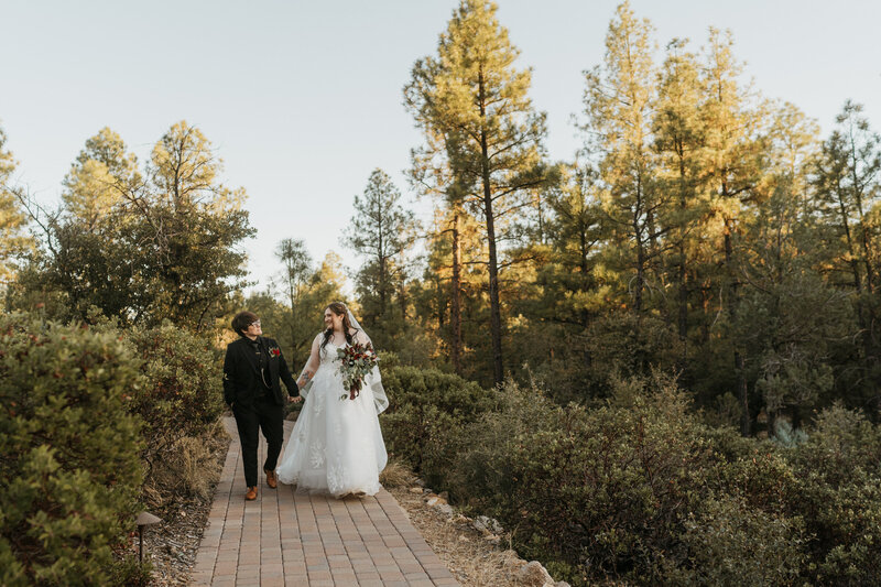 A newlywed couple holding hands and walking along a path in a garden 