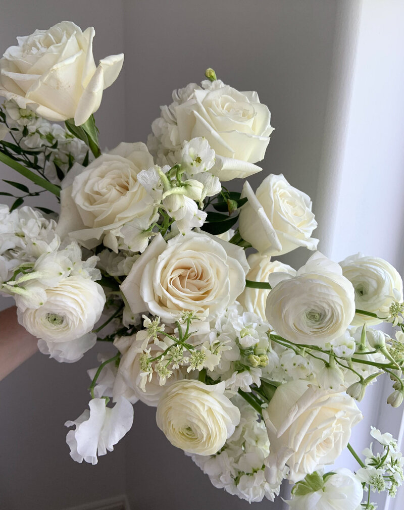 White monochromatic wedding flowers bouquet with roses, sweet pea, ranunculus, stock, delphinium, and orlaya lace.