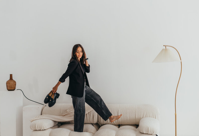 Walking on air (or a plush couch), like I own the place, rocking black barrel jeans, a sleek blazer, and black Coach loafers. Glancing back with a look that says, "Yeah, I totally meant to do that" as I glide across this plush white couch exuding boss energy