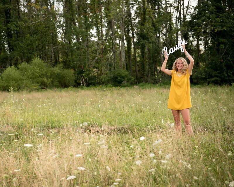 senior girl holding laugh sign in flower field