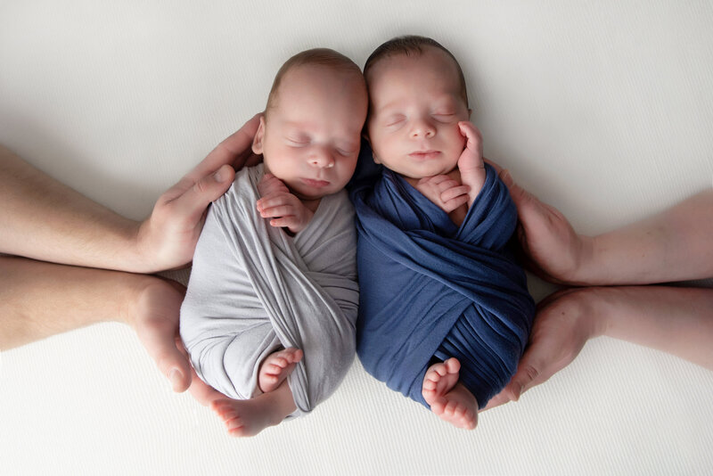 Newborn Twin Boys swaddled and photographed together in parents hands.