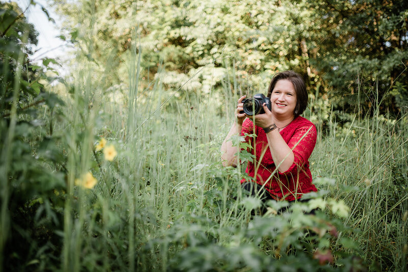 branding photo of a Philadelphia wedding photographer holding digital camera and smiling in tight shot with ivy on one side